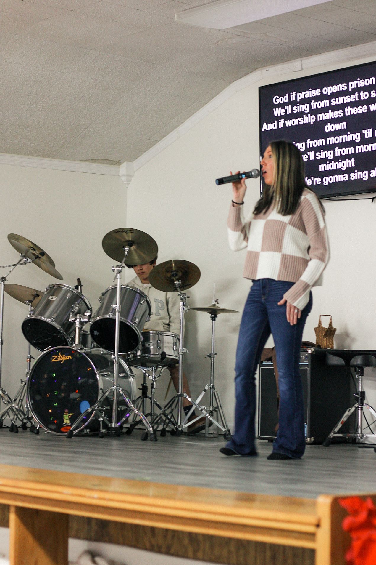 A woman singing into a microphone in front of a drum set