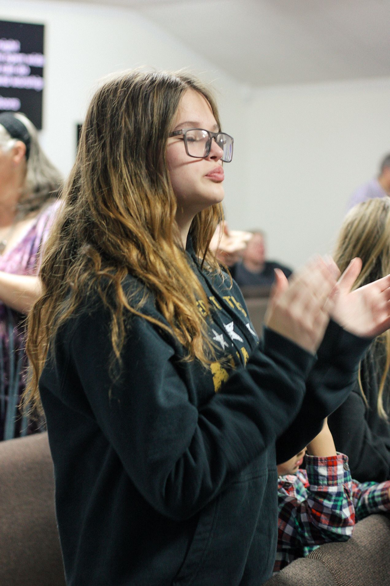 A young woman wearing glasses is clapping her hands in a church.