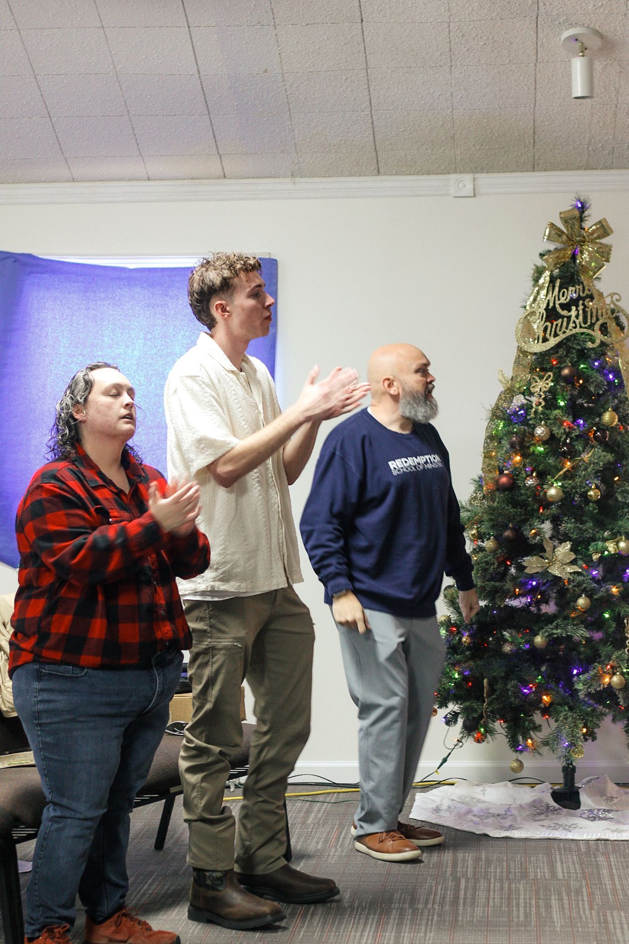 Three men are standing in front of a christmas tree.