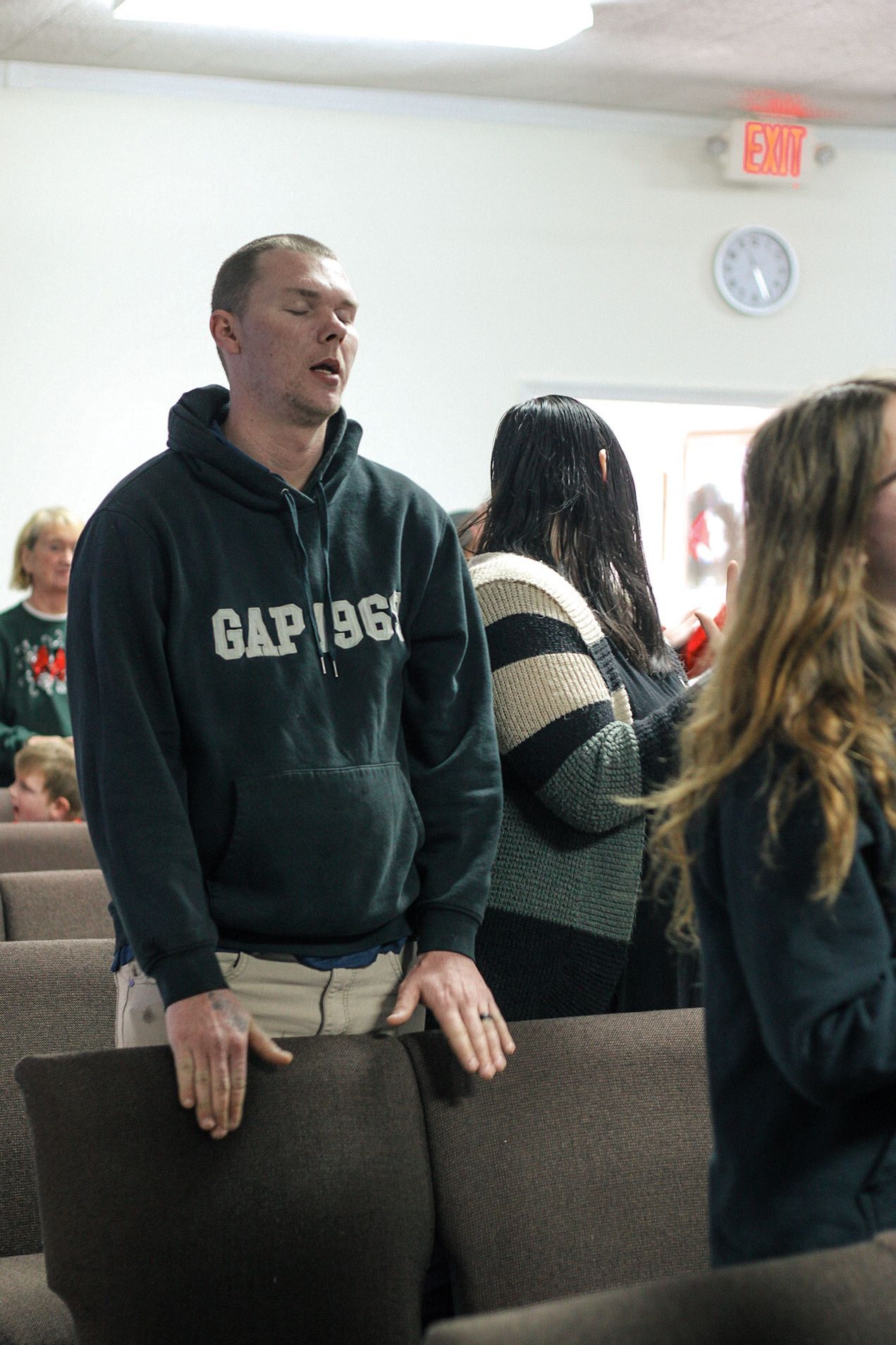 A man wearing a gap sweatshirt is standing in front of a group of people.