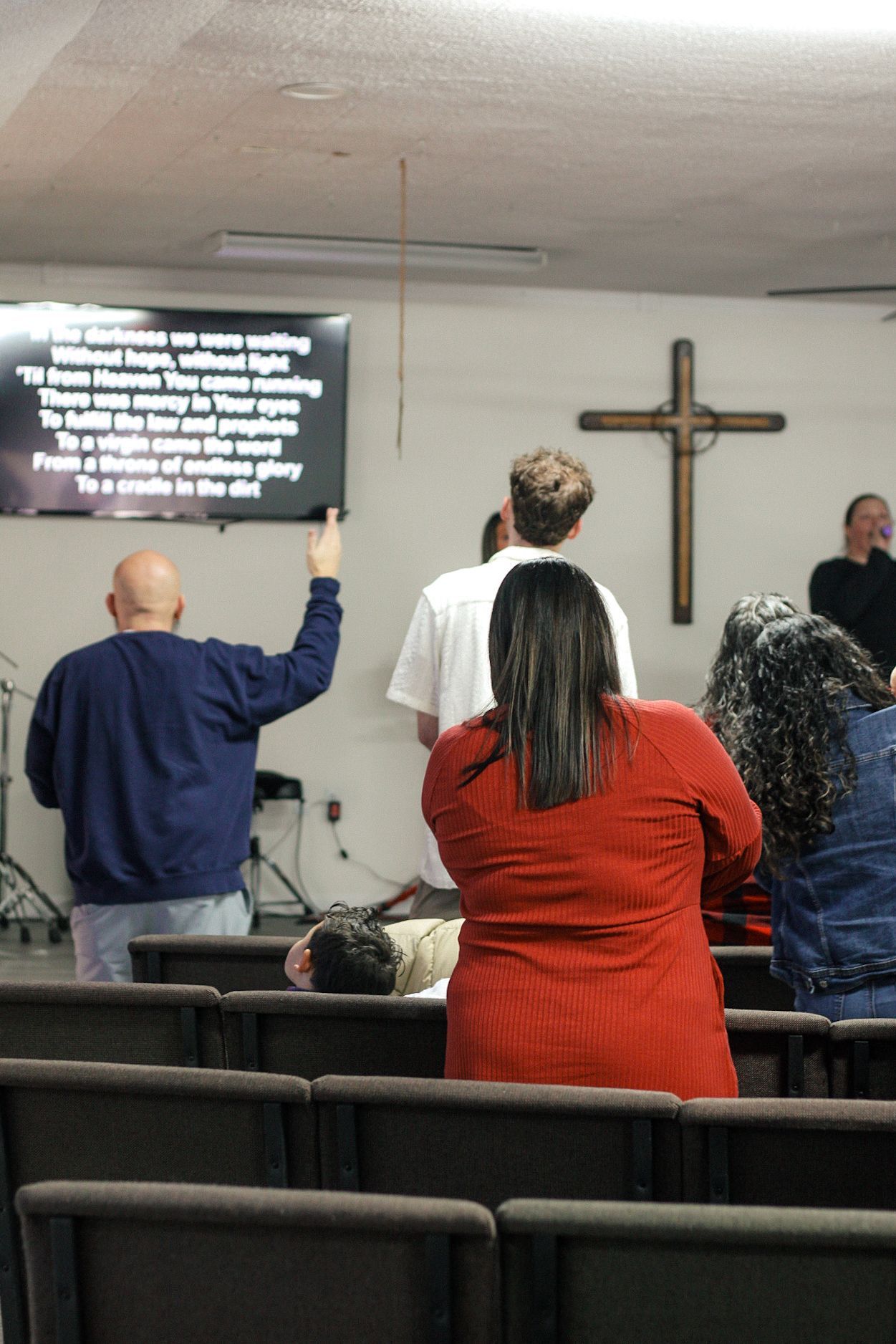 A group of people are sitting in a church with a cross on the wall.