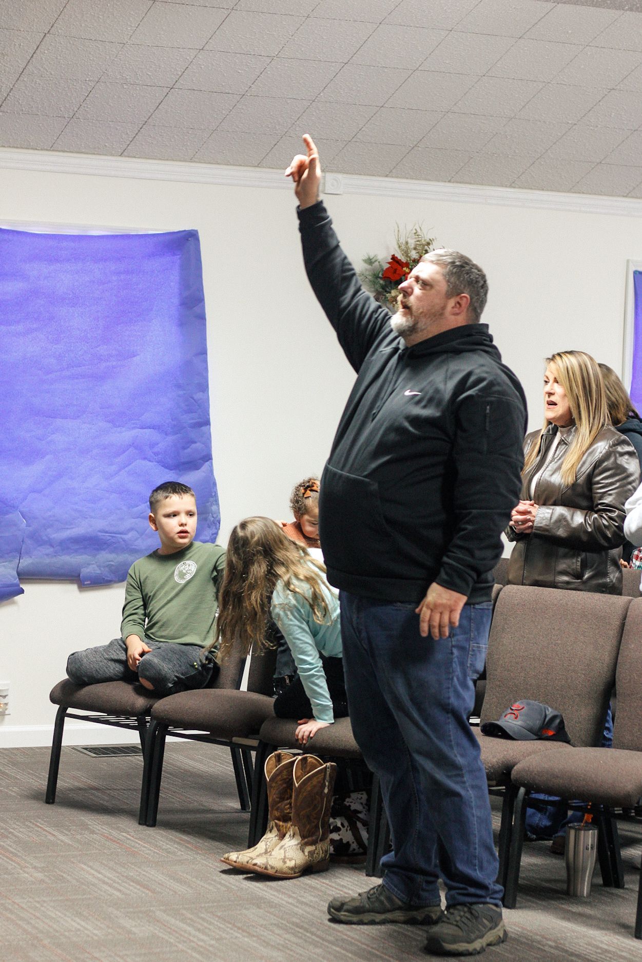 A man is standing in front of a group of people and pointing up.