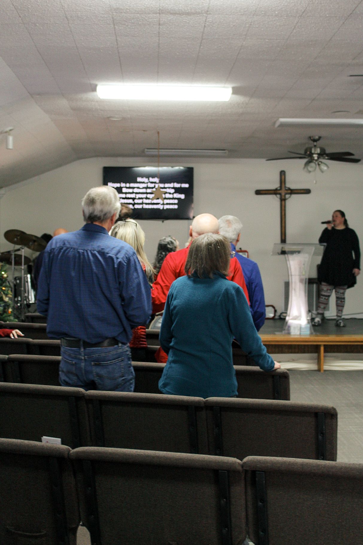 A group of people are sitting in a church with a cross on the wall.