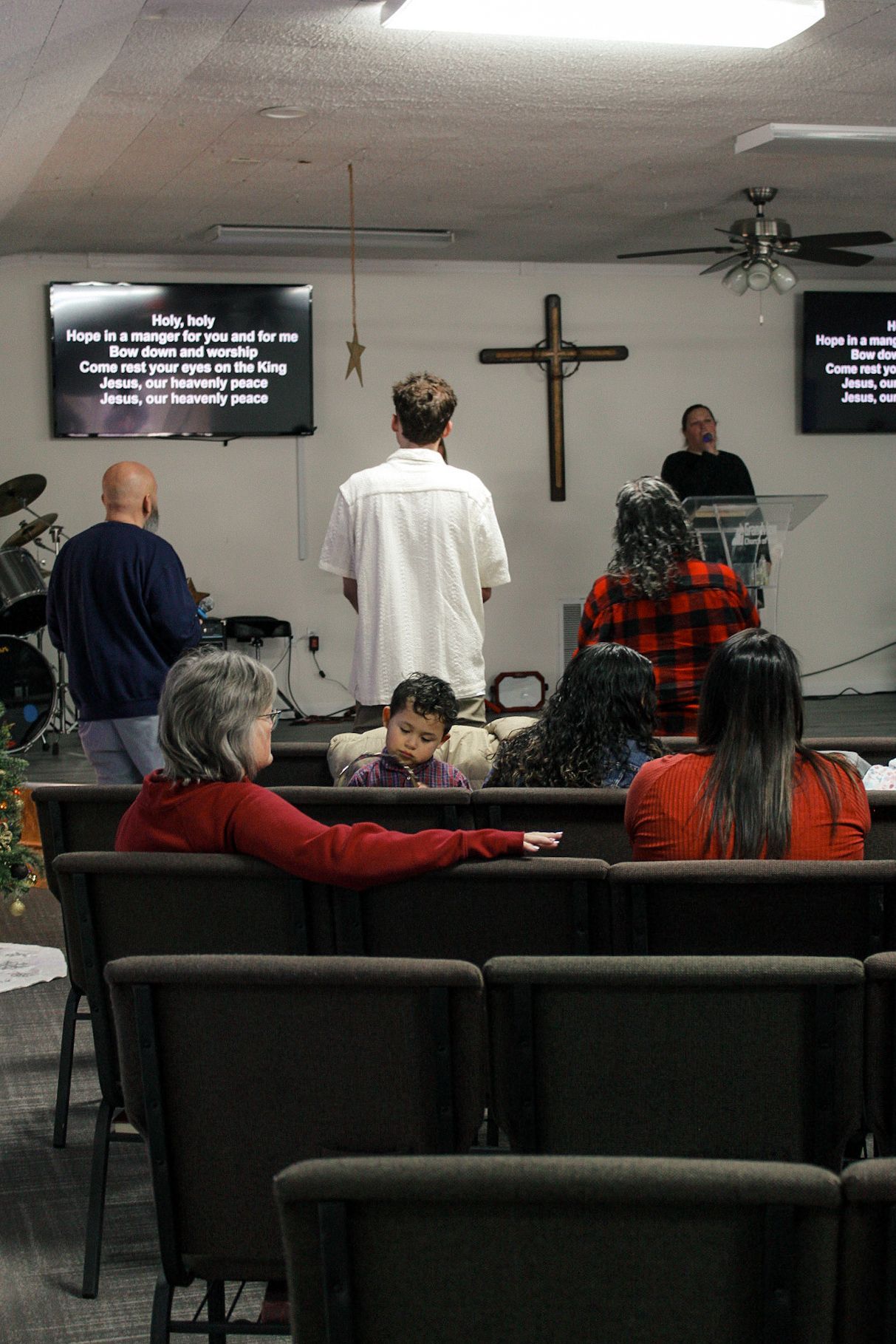 A group of people are sitting in a church with a cross on the wall.