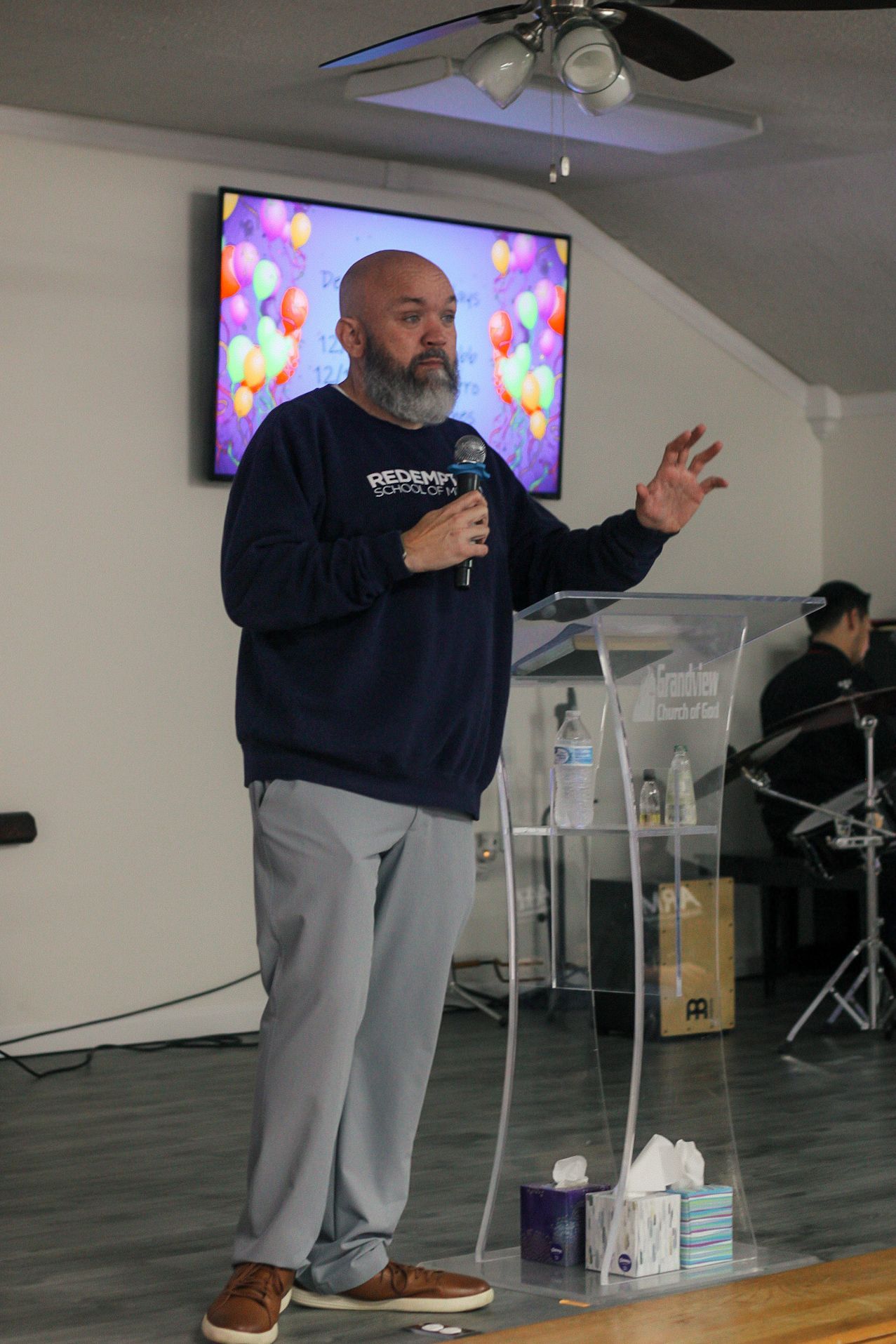 A man with a beard is standing at a podium holding a microphone.