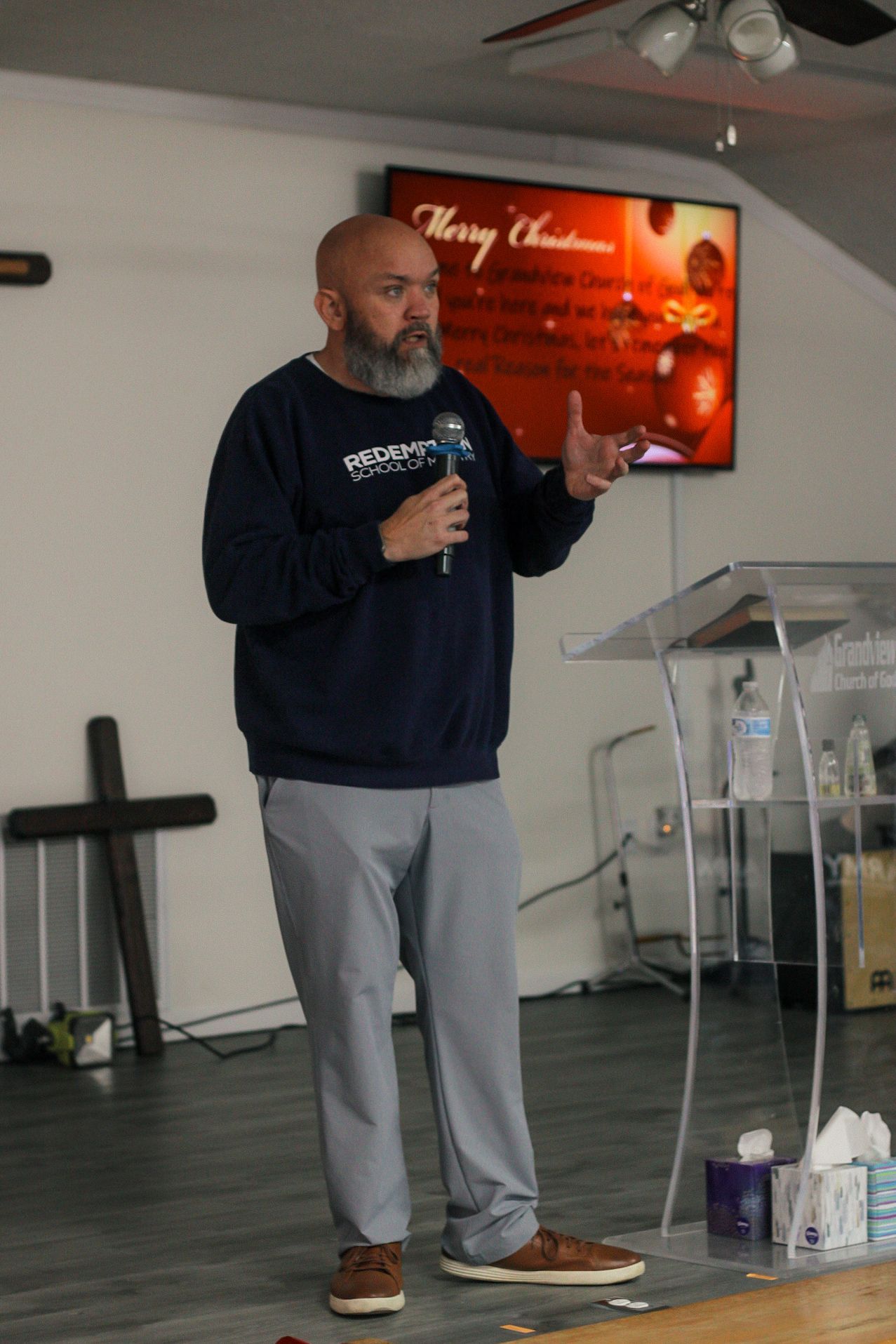A man with a beard is standing in front of a podium holding a microphone.