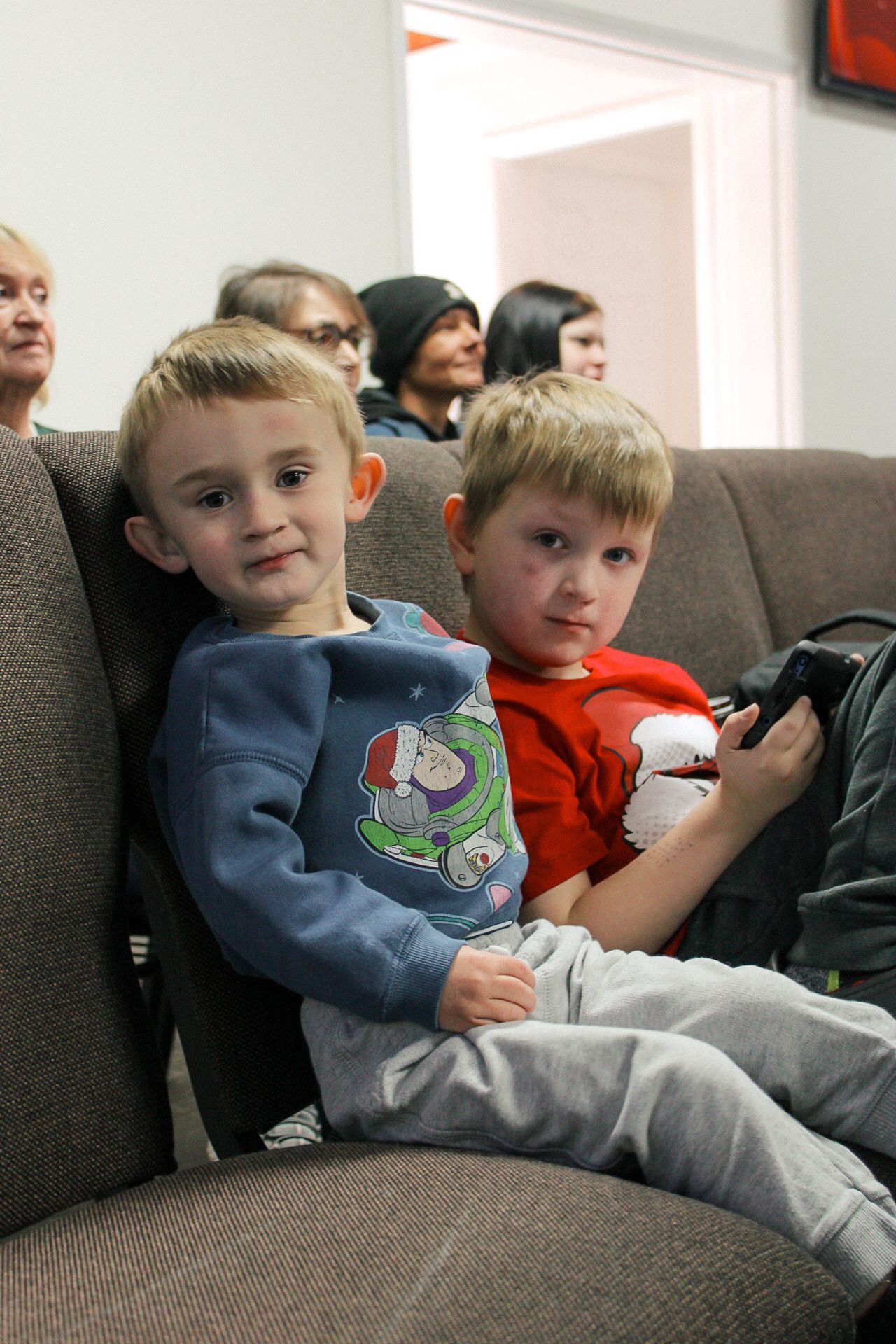 Two young boys are sitting on a couch watching a movie.
