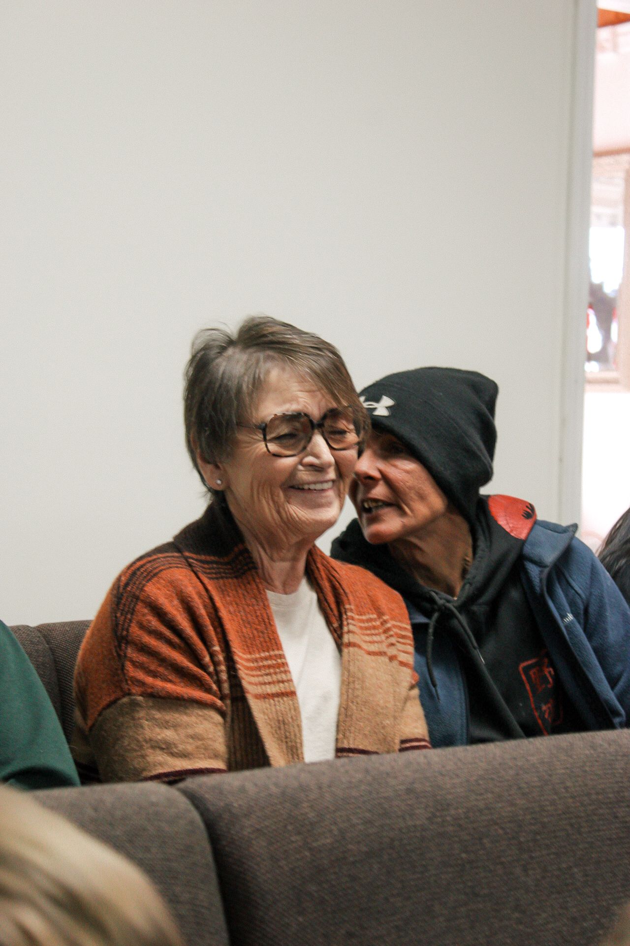 Two older women are sitting on a couch and smiling.
