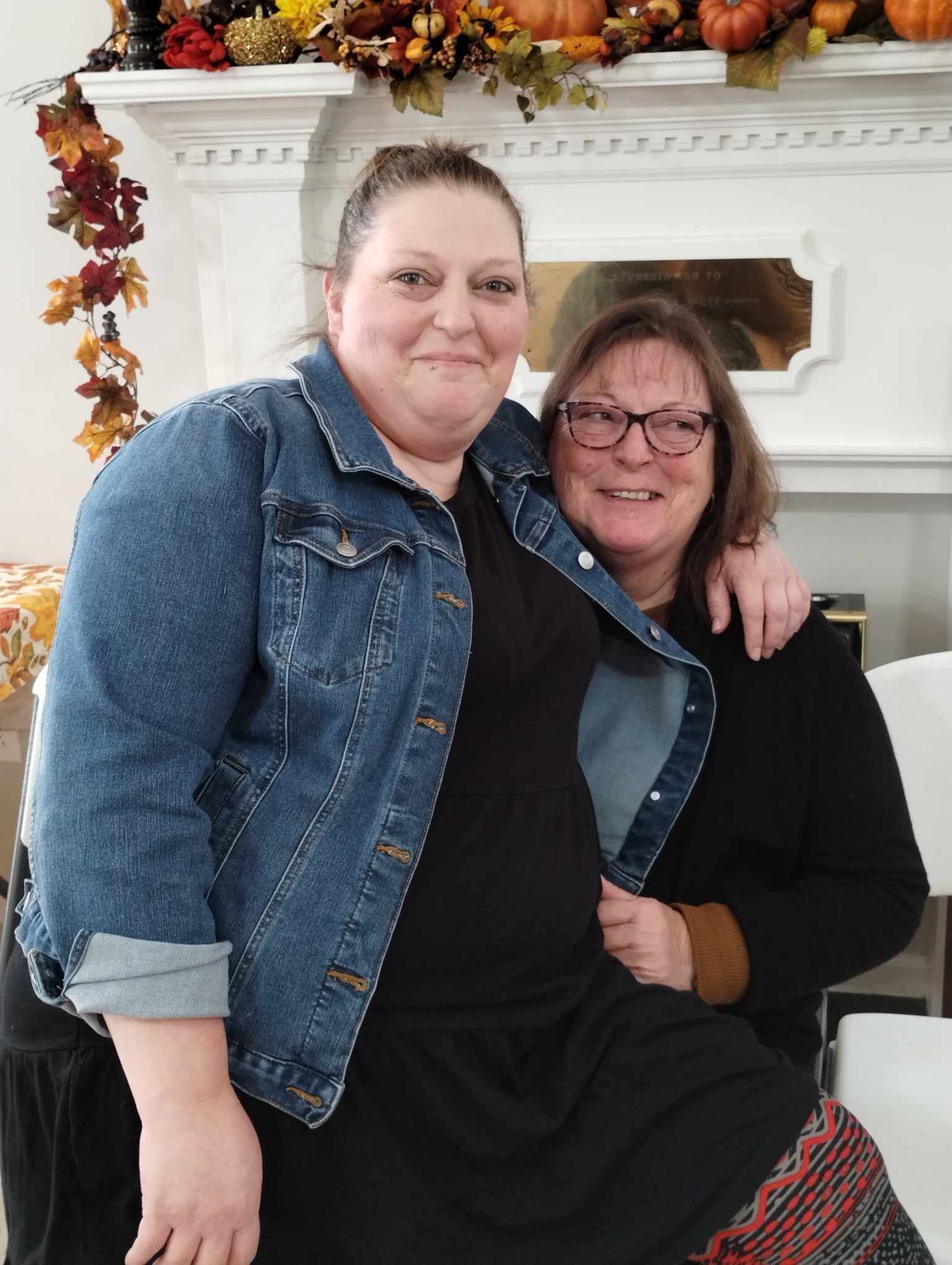 Two women are posing for a picture in front of a fireplace.