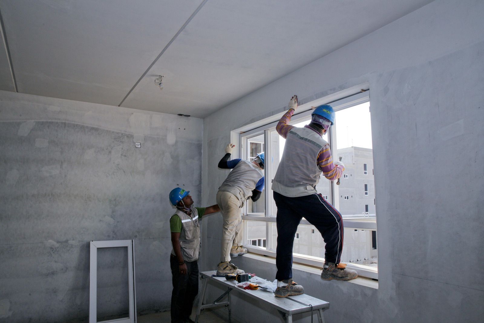 Three construction workers installing trim around a window in a room under construction.
