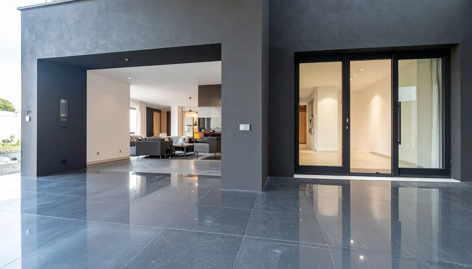 Exterior view of a modern building with a glossy dark floor, open interior, and glass sliding doors.