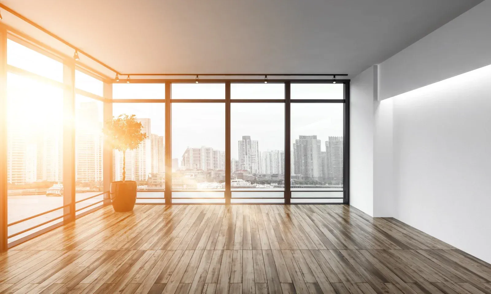 Empty modern room with large windows, city view, and wood floor. Bright sunlight.