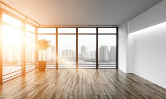 Empty modern room with large windows, city view, and wood floor. Bright sunlight.