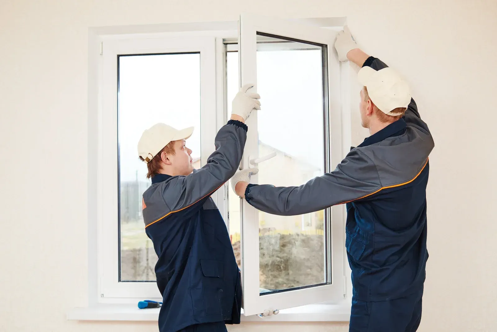 Two workers in blue uniforms install a white window.