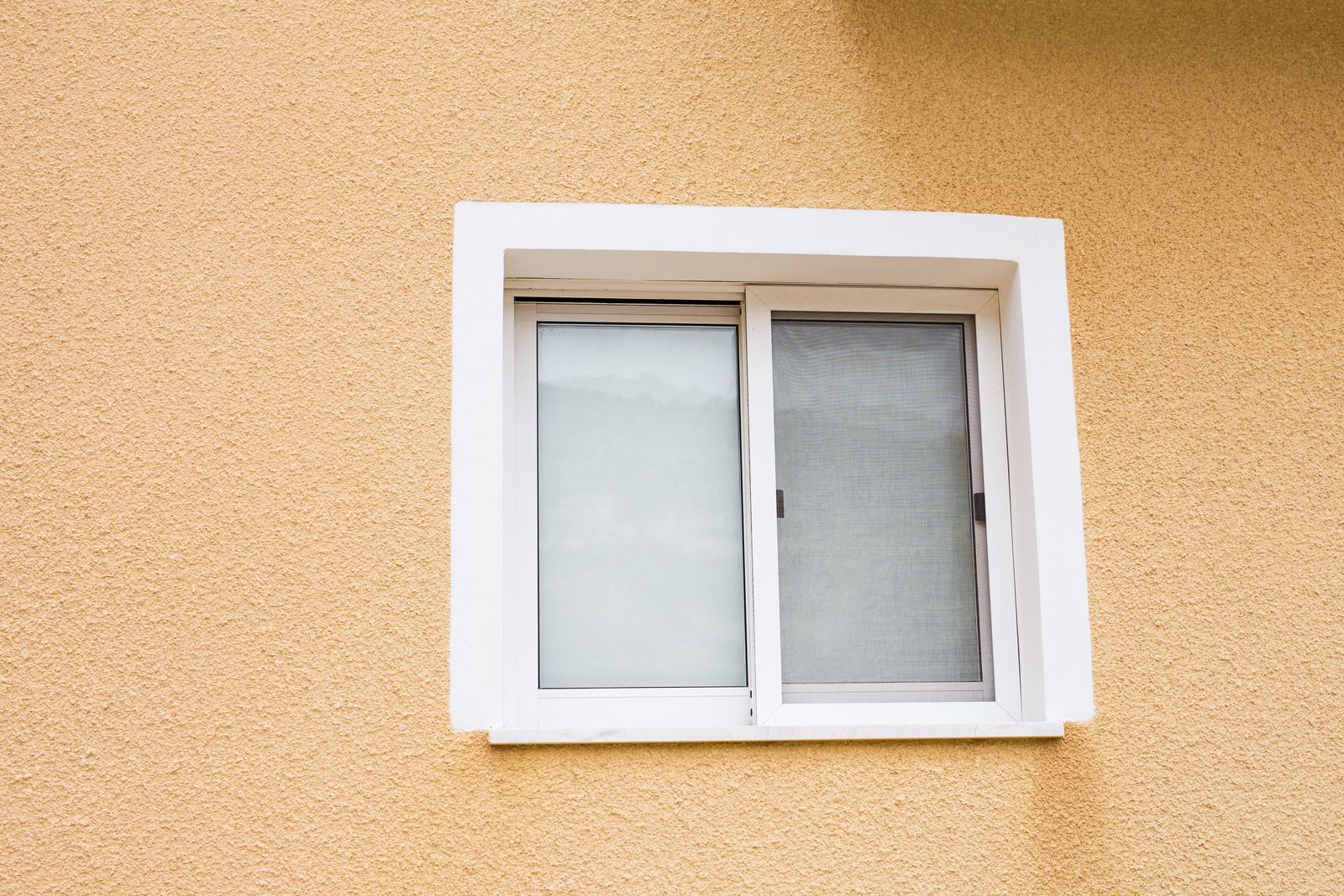 Person installing window. Wearing gloves, green shirt, and overalls, sky visible through window.