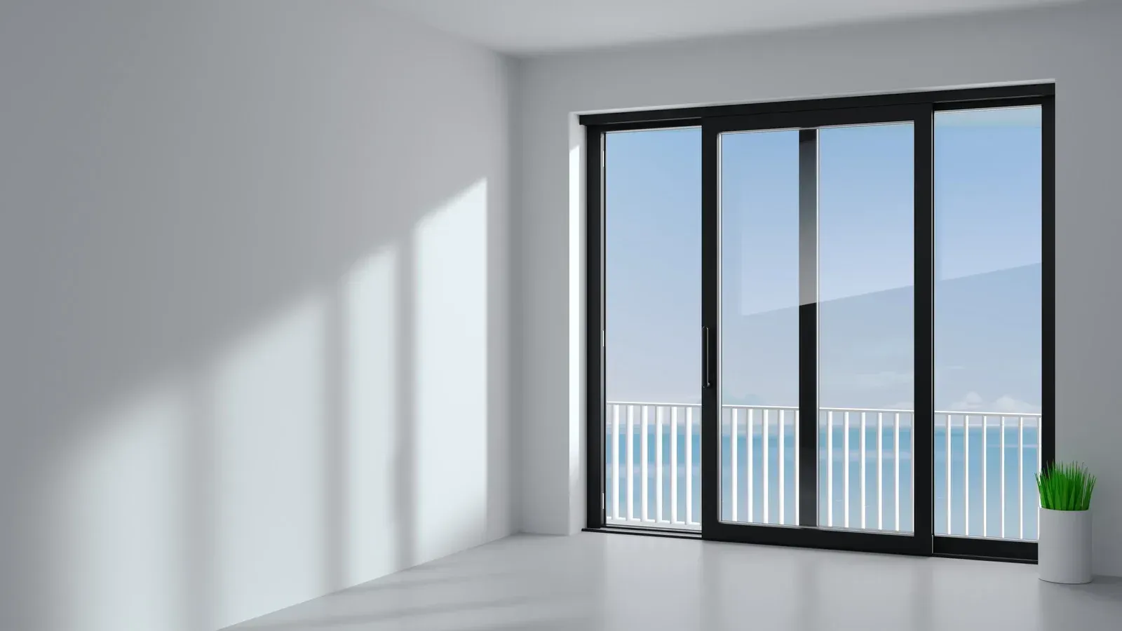 Empty white room with black framed sliding glass door overlooking a white railing and ocean view.