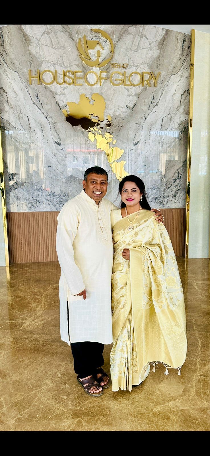 A couple smiling while standing in front of a decorative, marble-patterned wall labeled 