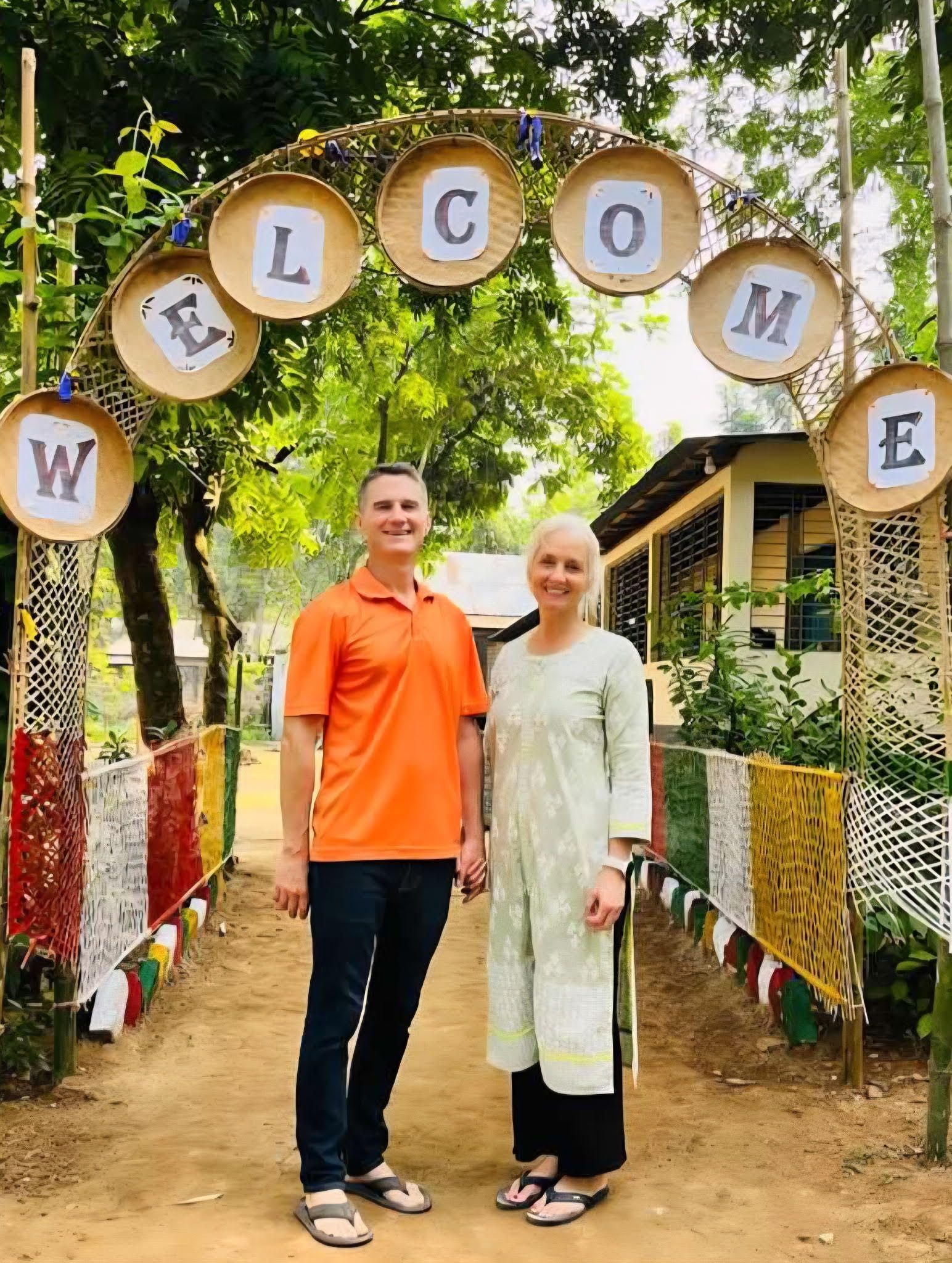 Christy and Kevin stand under a bamboo archway with circular signs spelling 