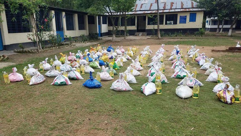 Many bags of relief aid arranged in rows on a grass field in front of a school building.