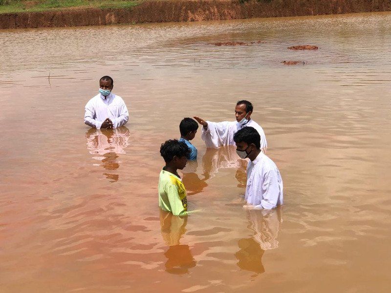 People in white shirts performing a Christian baptism in an outdoor, muddy body of water.