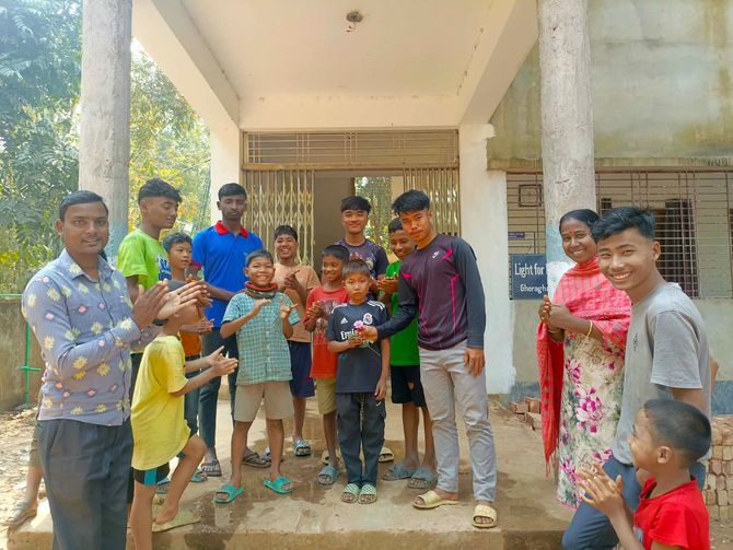 A group of people standing together in front of a building, some clapping and smiling.