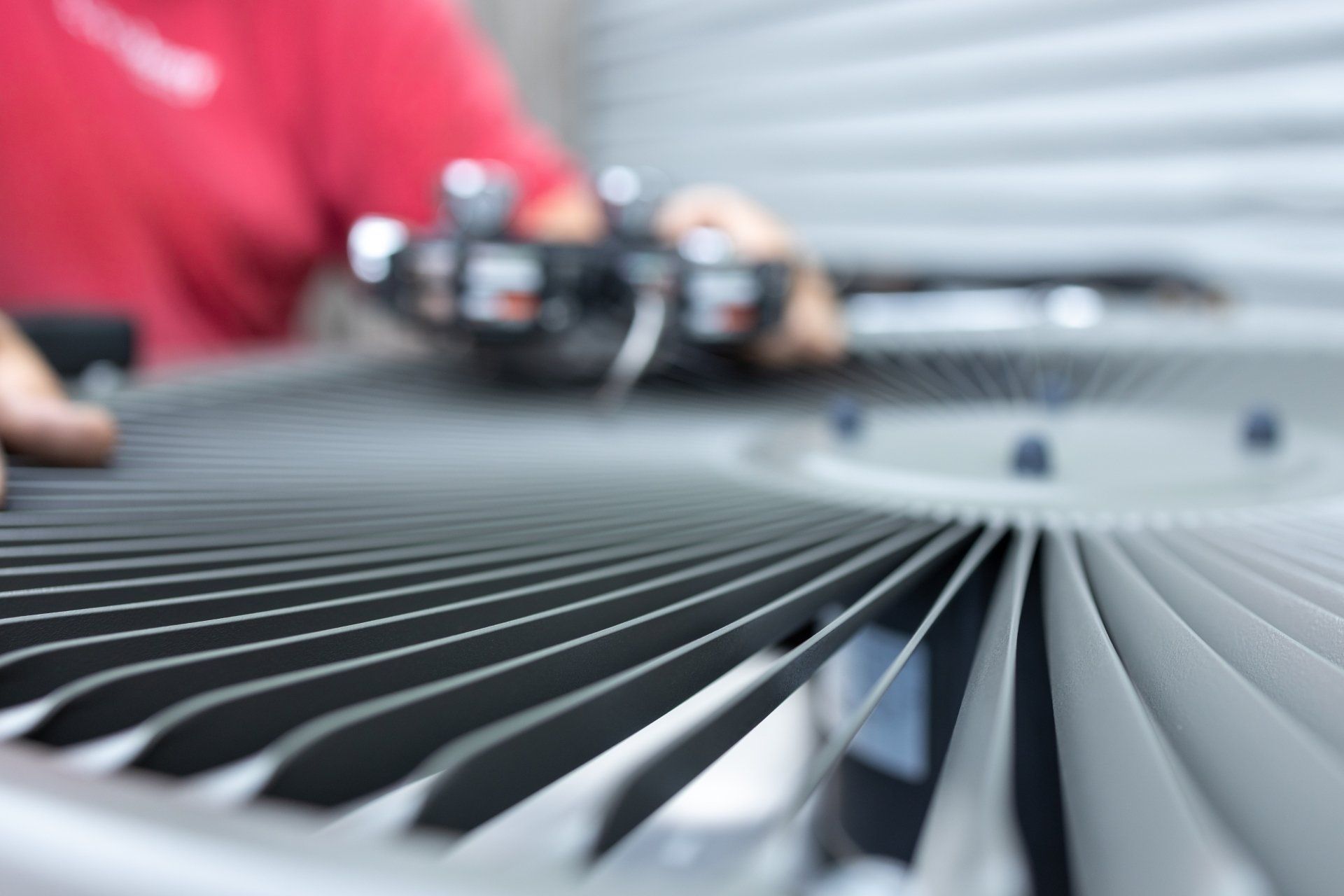 Person repairing an air conditioner unit, close-up on the fan with silver blades.