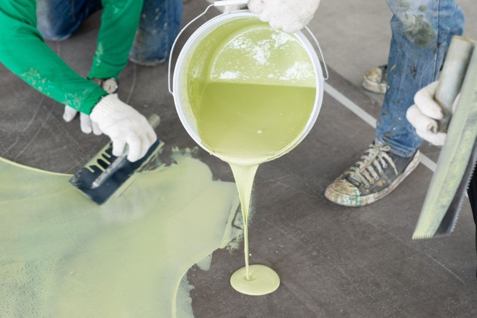 A person is pouring paint from a bucket onto a floor.