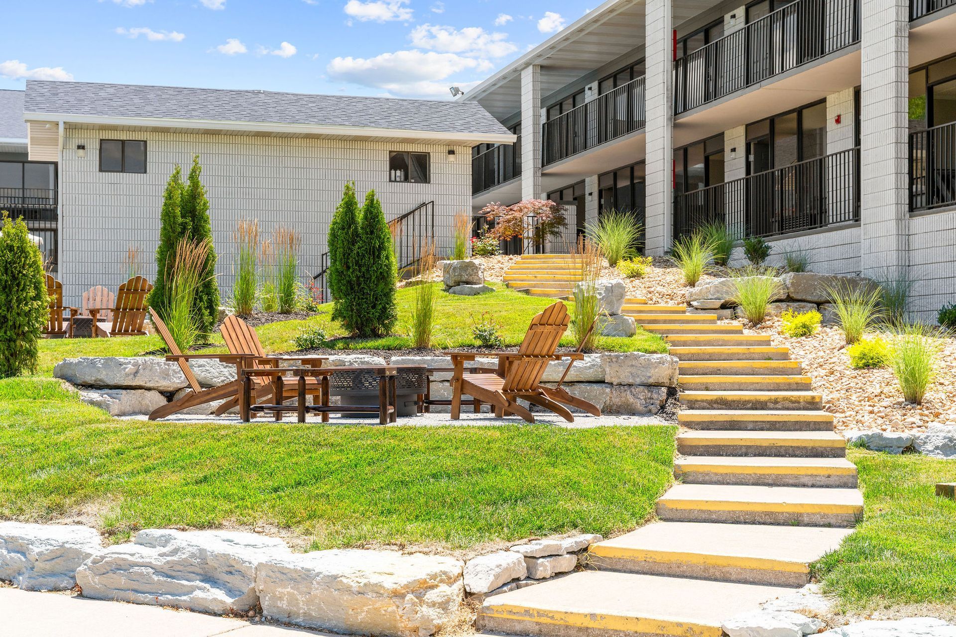 There are stairs leading up to a building with a fire pit and chairs in front of it.