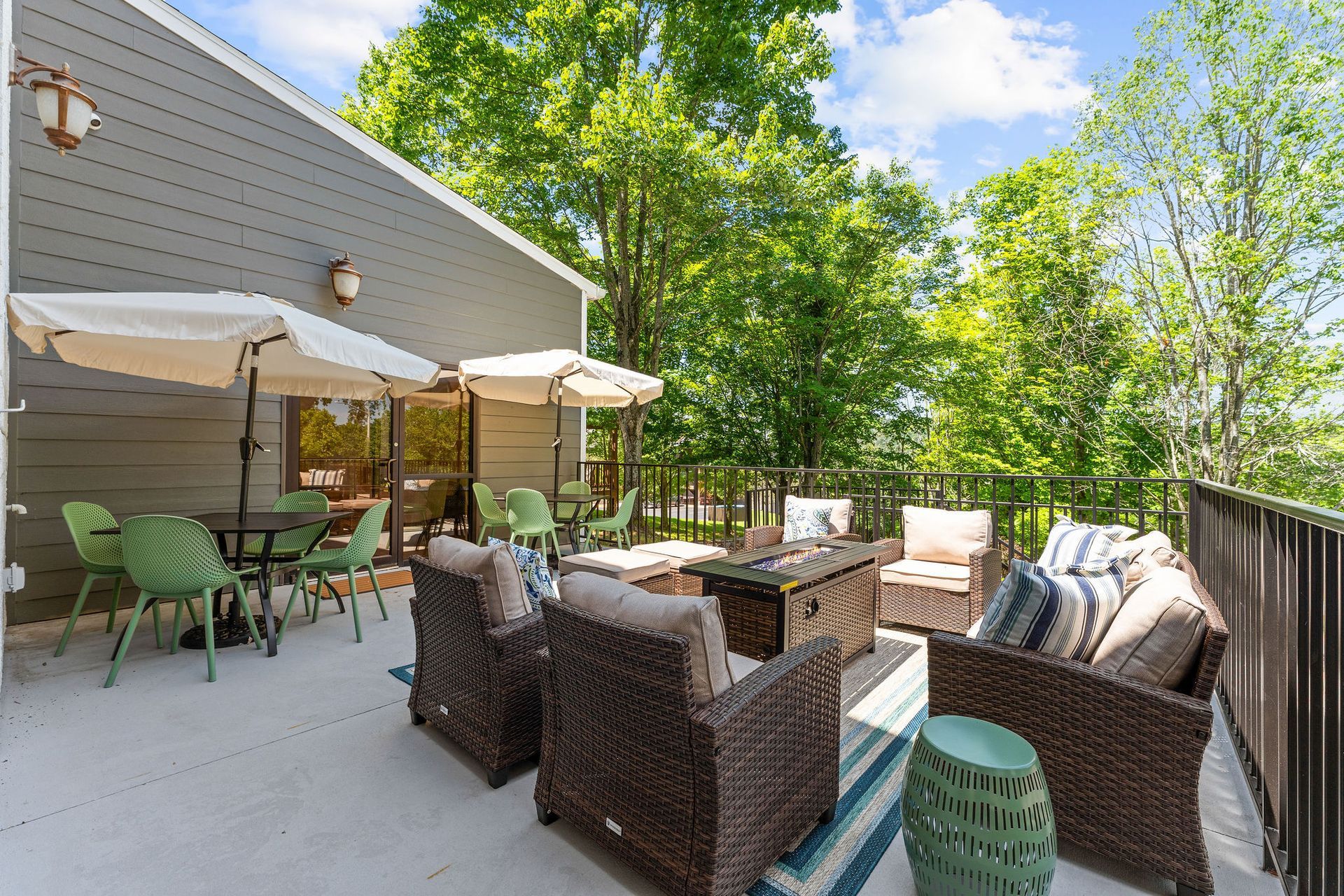 A patio with chairs , tables , umbrellas and a fire pit.
