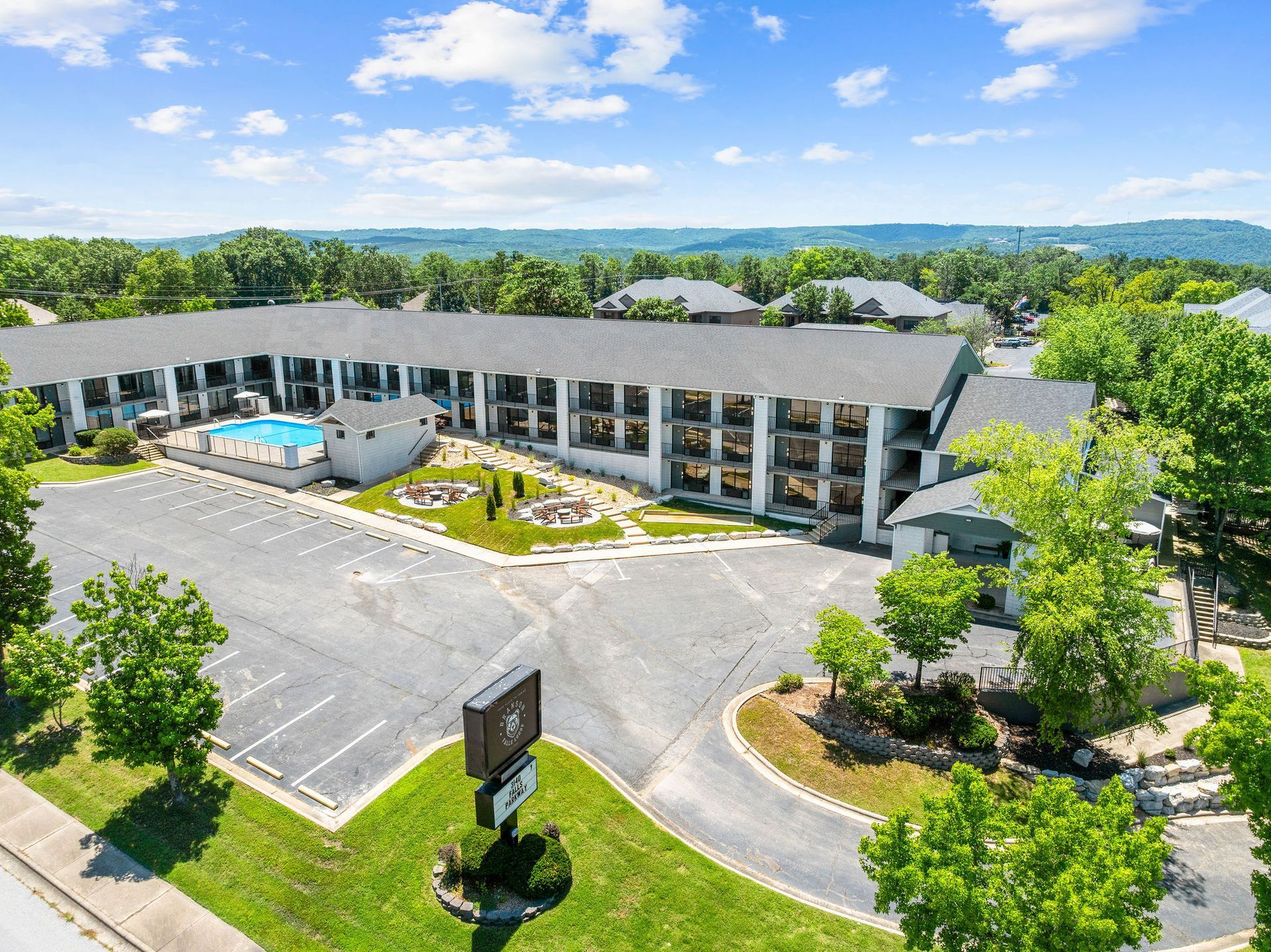An aerial view of a hotel with a swimming pool surrounded by trees.