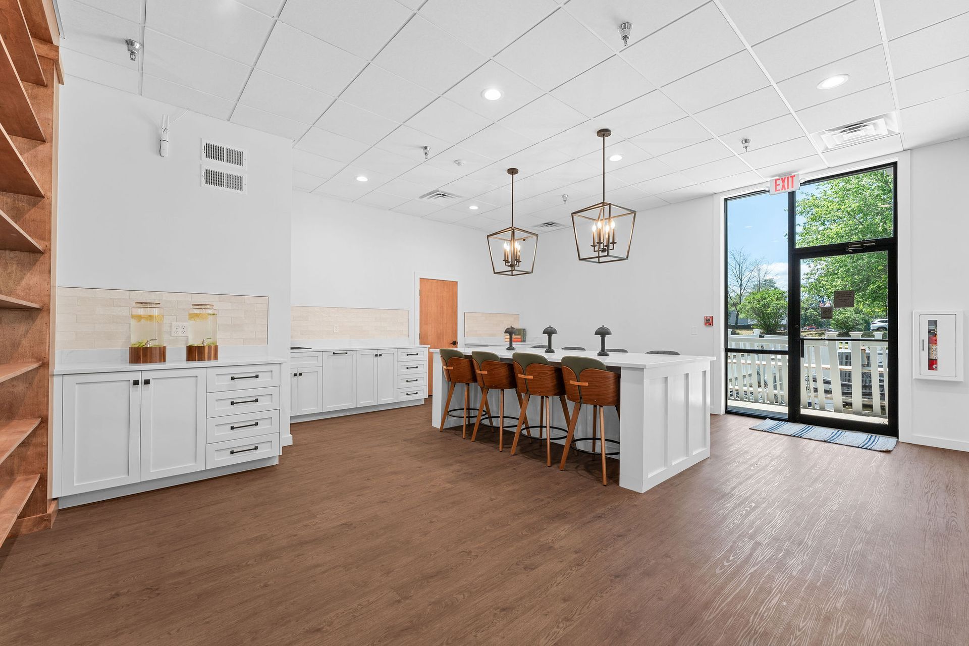 A kitchen with white cabinets , wooden floors , stools and a large window.