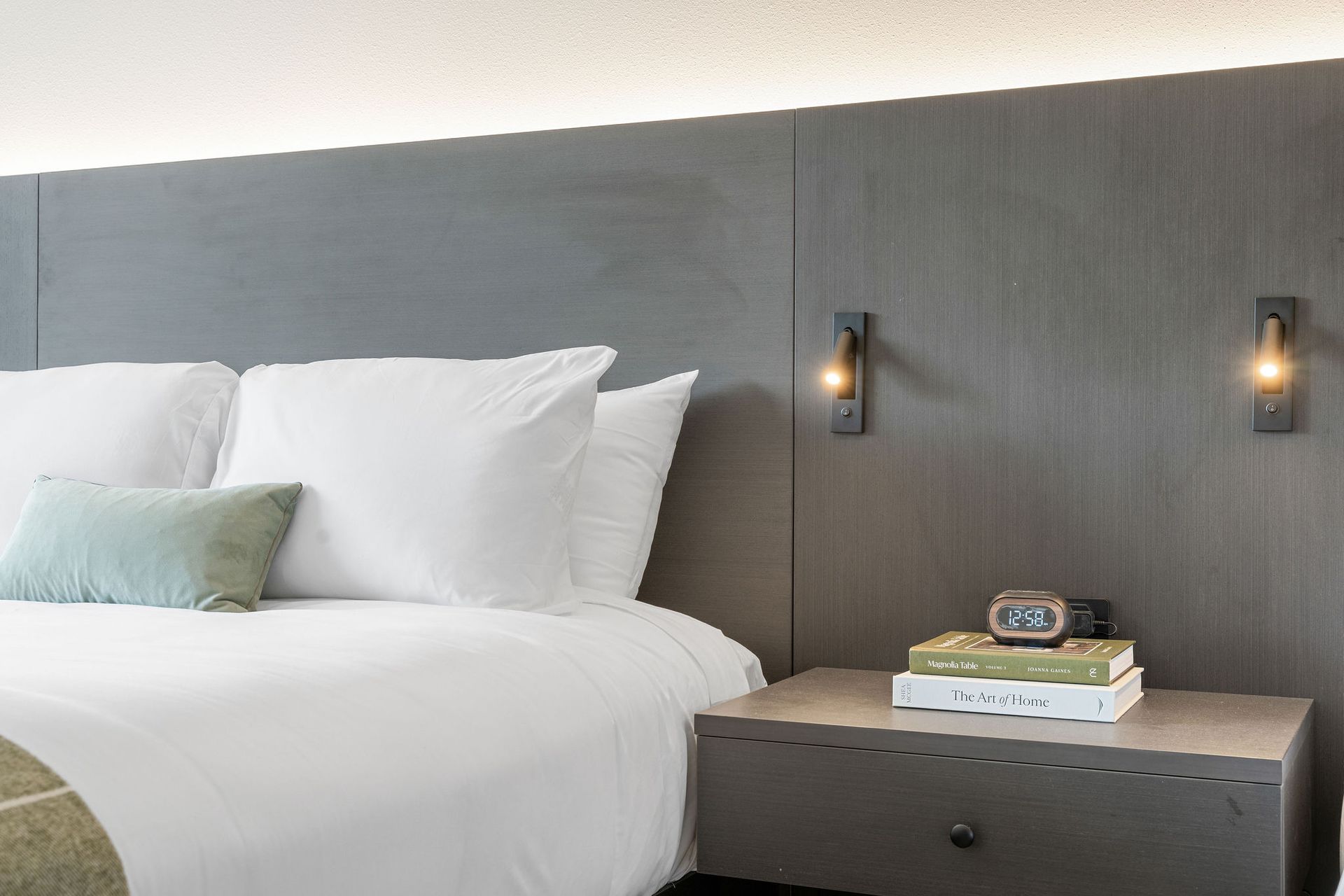 A hotel room with a bed and a nightstand with a clock on it.