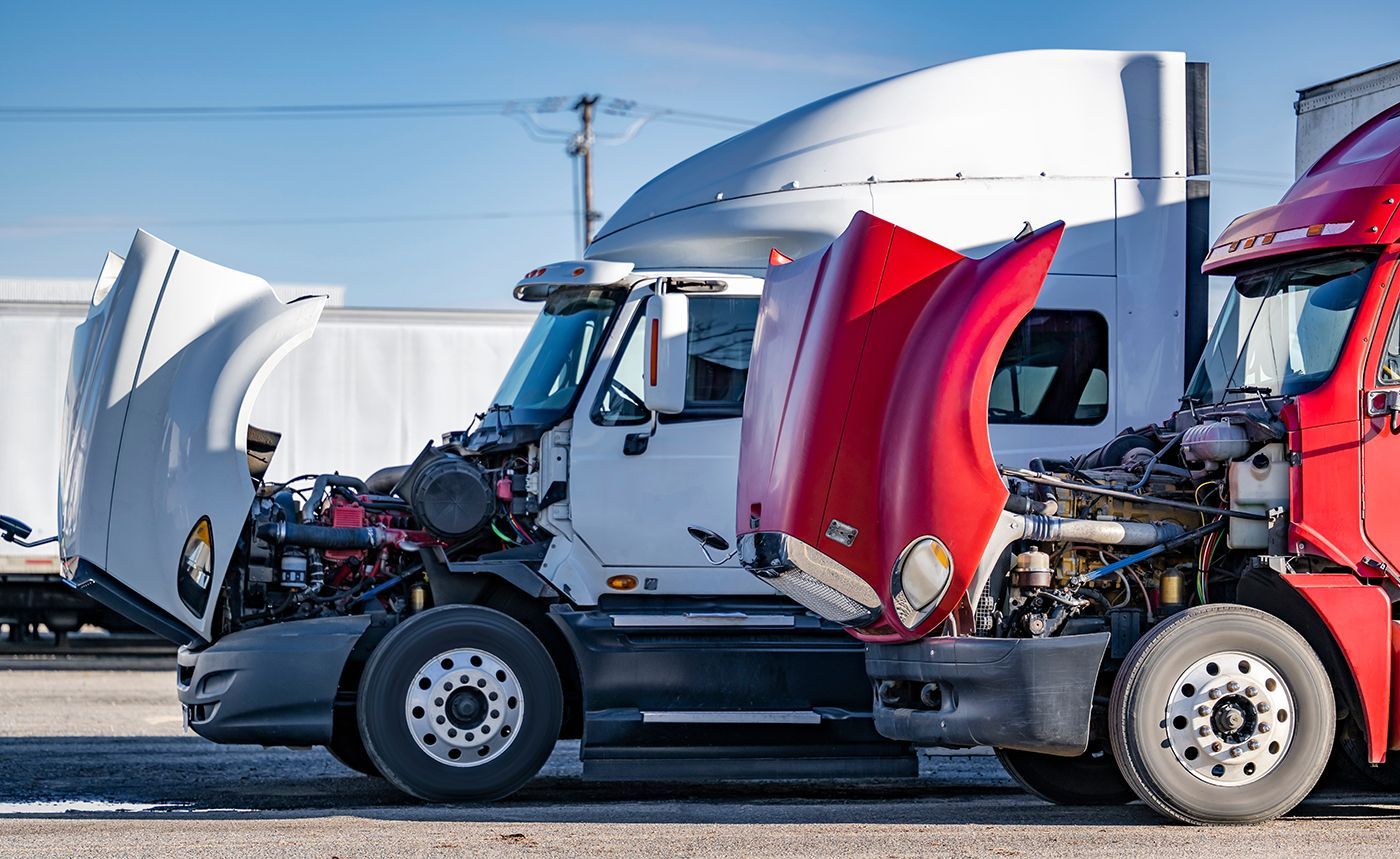 White and red semi-trucks with their hoods up, parked outside on a sunny day.