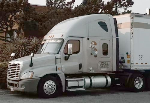 Silver semi-truck with a Mario decal on the side parked outside, next to a building.
