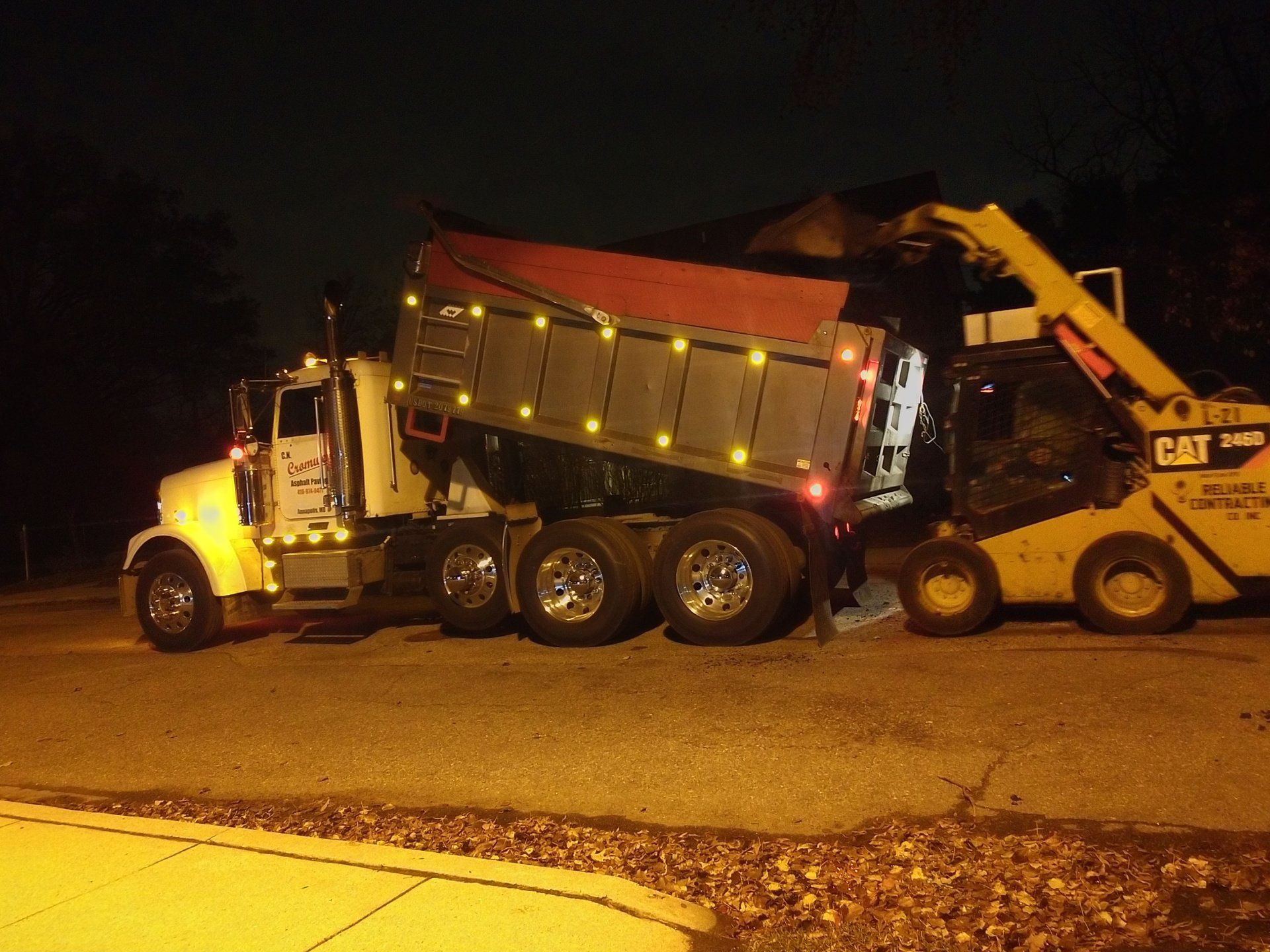 large dump truck being loaded by an excavator at night on a construction site, illuminated by their lights.