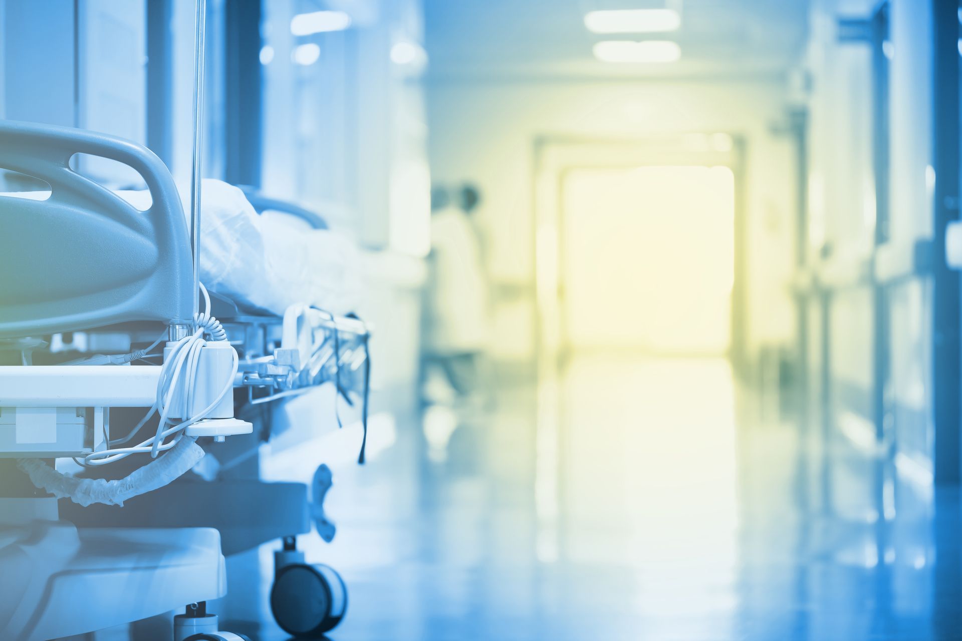 A hospital hallway with a bed and a nurse in the background.