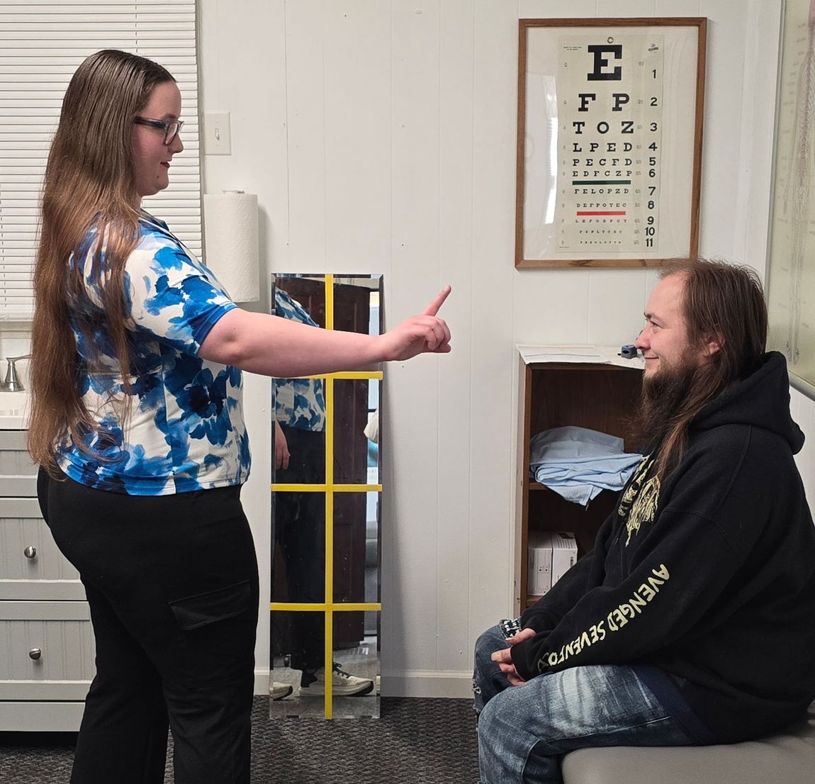 A woman giving a man a thumbs up in front of an eye chart