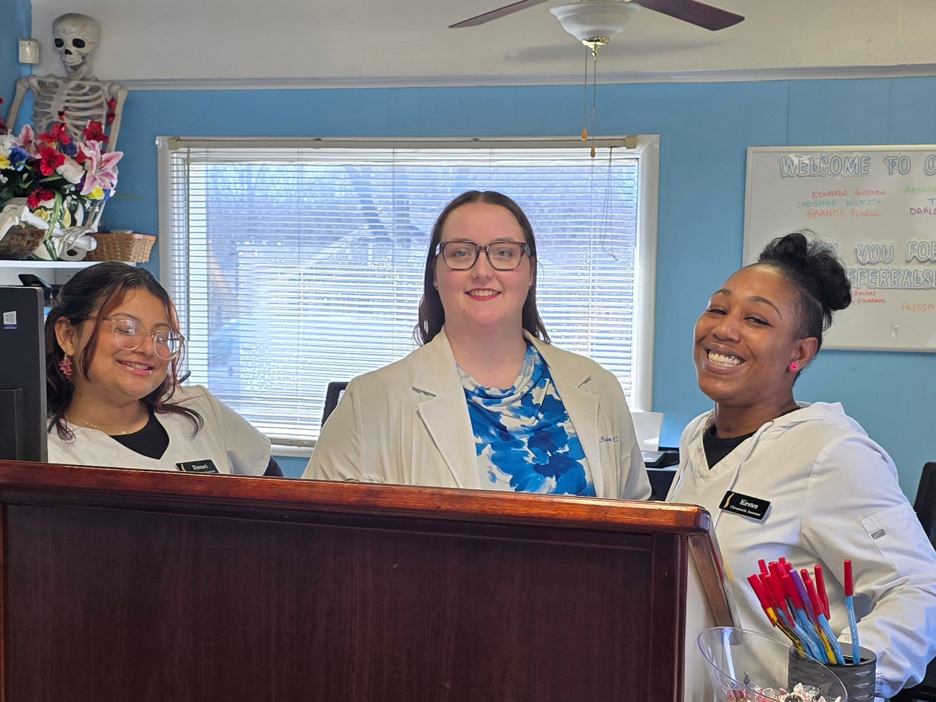 Three women are standing behind a counter in a dental office.