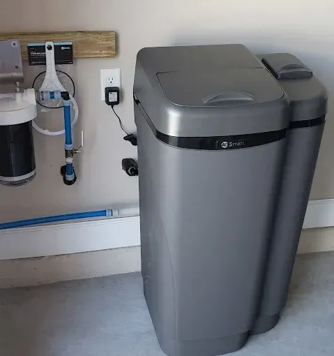 A water softener system in a garage setting, with a filter, pipes, and electrical outlet.