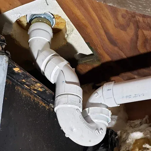 White PVC pipe plumbing snaking through a wooden structure, likely for drainage.