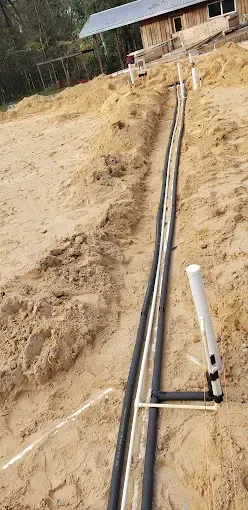 Pipes laid in a trench in the sandy ground near a building under construction.