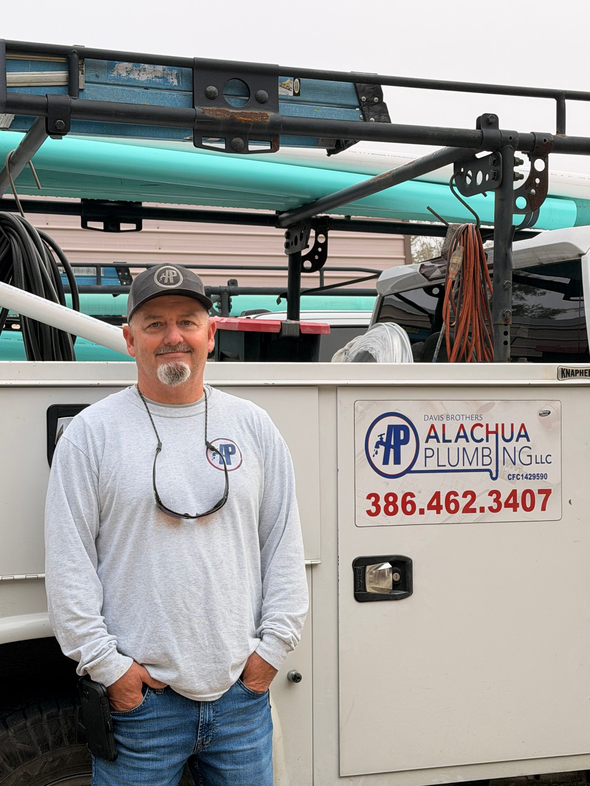 Man in front of a work truck with the Alachua Plumbing logo, smiling, hands in pockets.