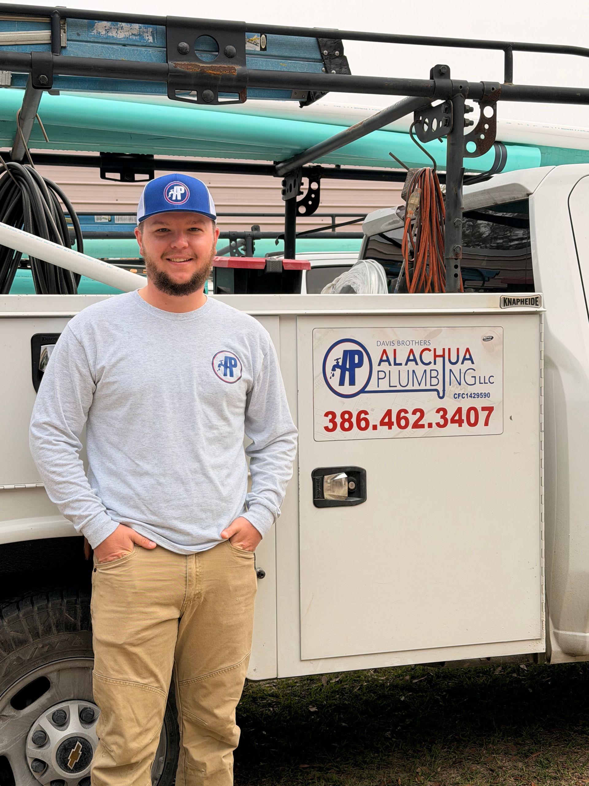 Man in a baseball cap and long-sleeved shirt, posing next to a plumbing truck with logo and phone number.