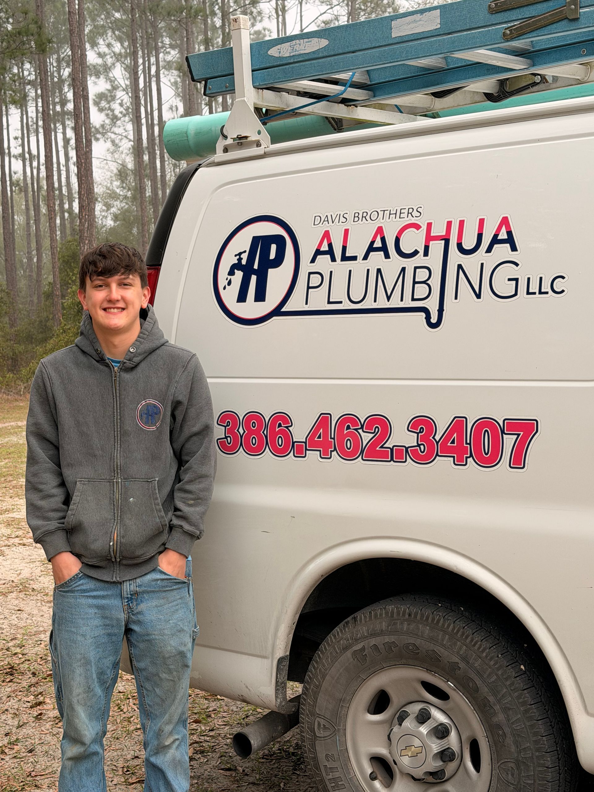 Man in front of a work truck with the Alachua Plumbing logo, smiling, hands in pockets.