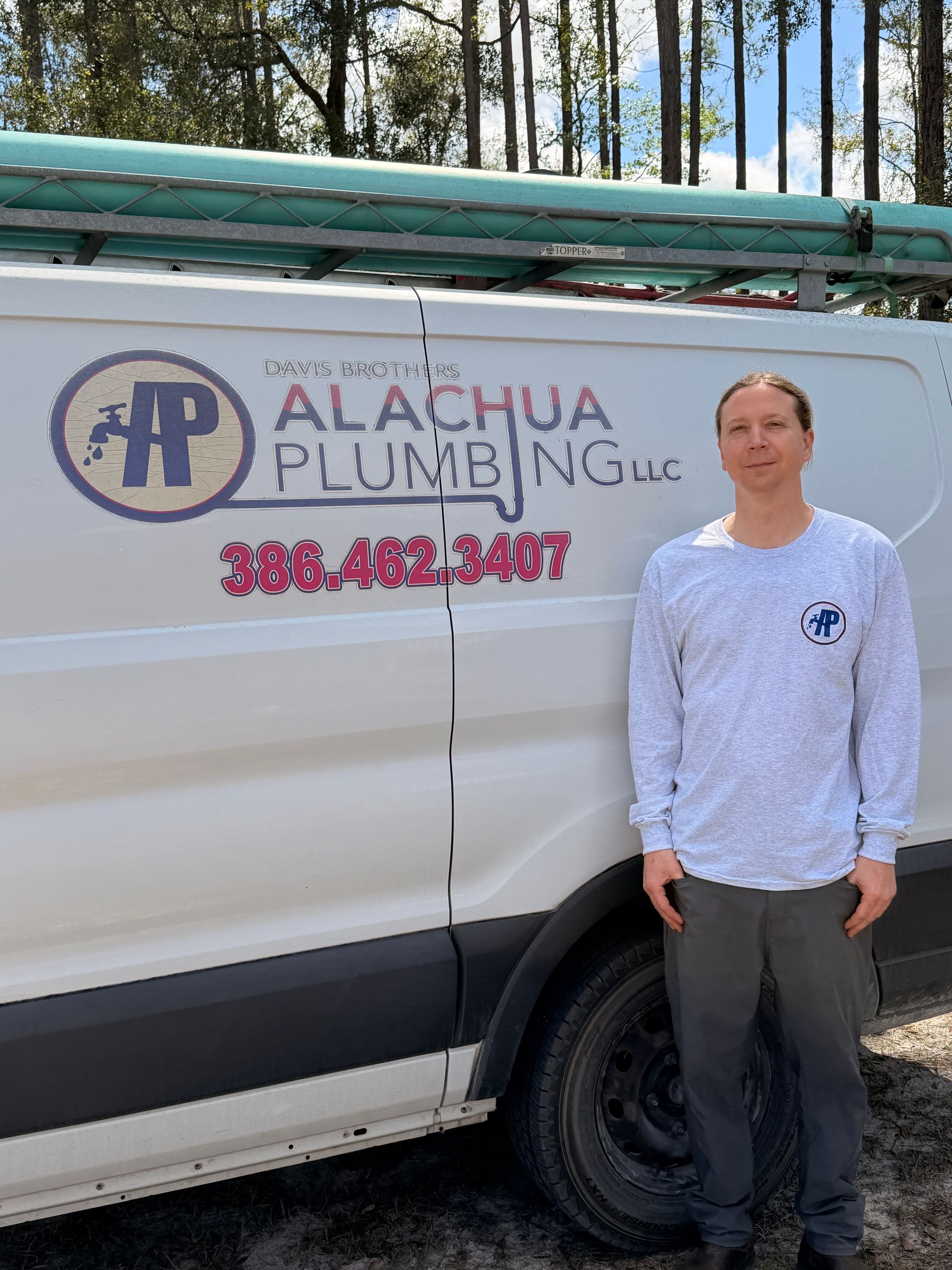 Man standing next to a white van with Alachua Plumbing logo and phone number.
