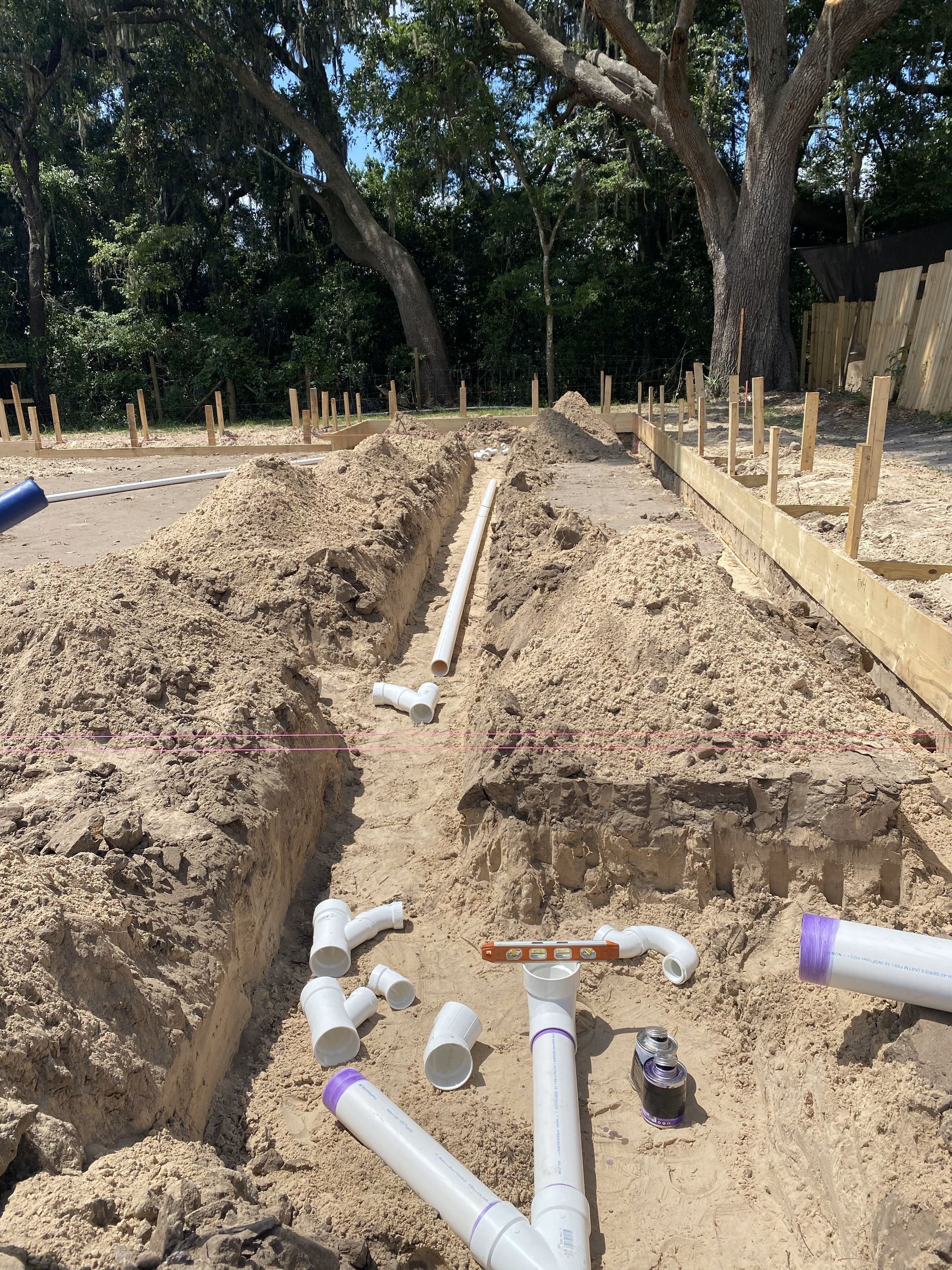 Trench with PVC pipes and fittings in sandy soil; construction site.