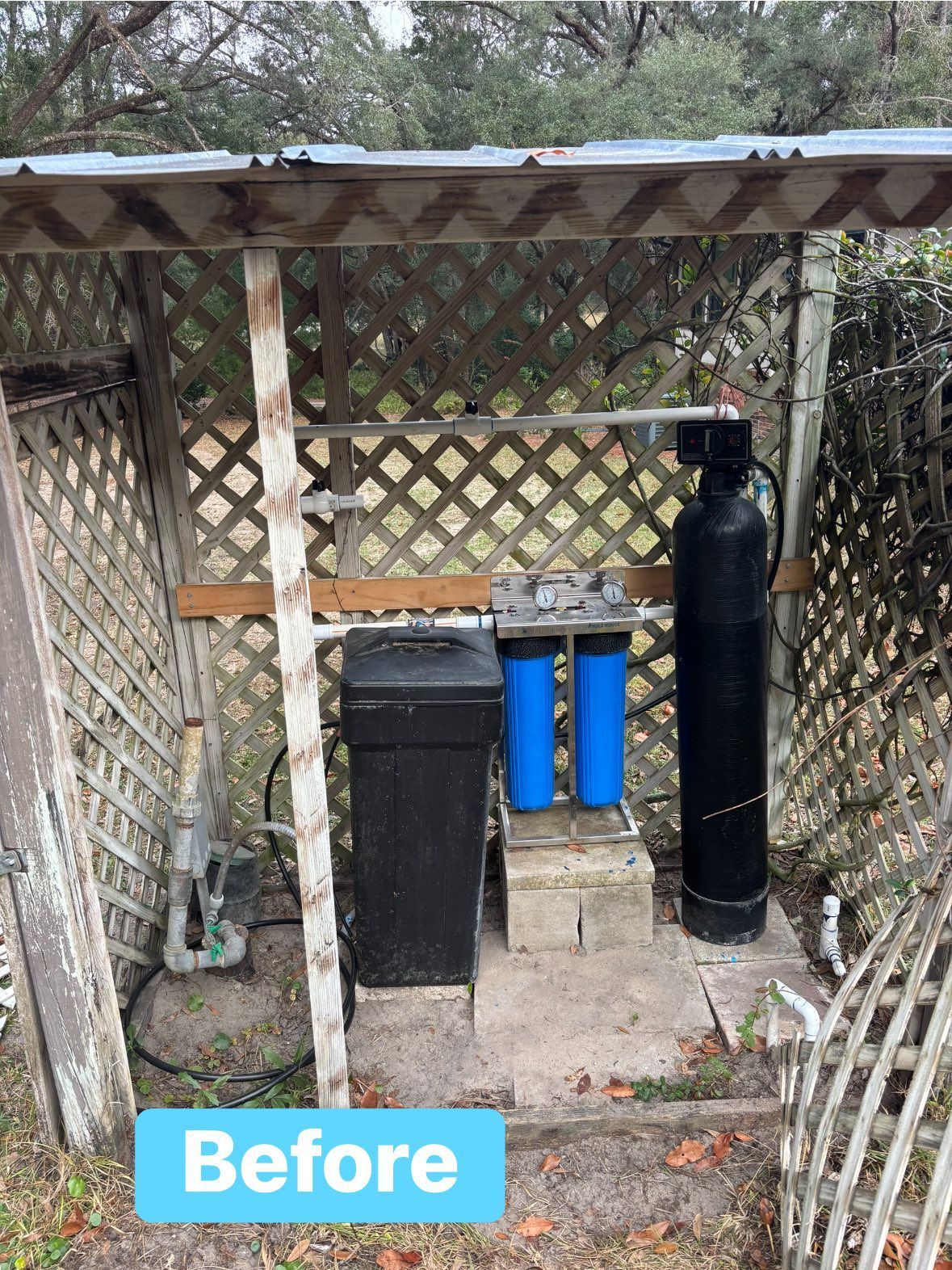 Outdoor water filtration system in a lattice enclosure; shows water softener, filters, and tank.