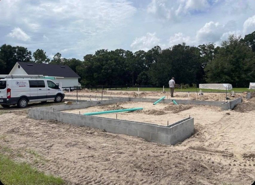 Construction site with concrete foundation and plumbing, white van, person standing.