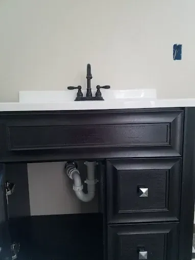 Black bathroom vanity with white countertop, faucet, and exposed plumbing.