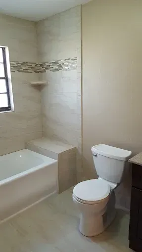 Bathroom with a white tub, toilet, and beige tile shower with a decorative mosaic accent.